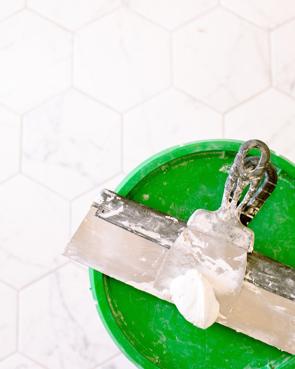 Drywall taping knives and joint compound on a mud bucket — repairs & maintenance by Valencia Ink
